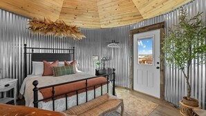 A bedroom with a bed, bedside table, lamp, and a view of the outside. - Southwest Silo Stay- 1 Bedroom Near Zion & Bryce (Fredonia)