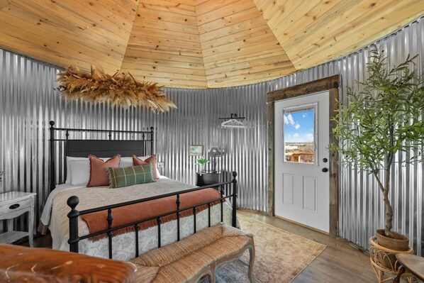 A bedroom with a bed, bedside table, bench, and a potted plant.