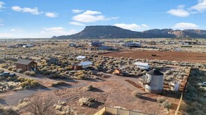 A rural landscape with sparse vegetation, a few buildings, and a prominent mountain in the background.