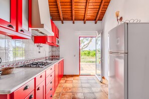 A kitchen with red cabinets, a white refrigerator, and a view to the outside.