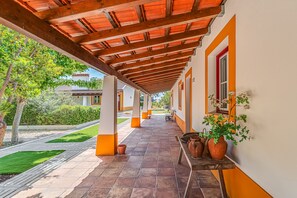 A covered outdoor corridor with tiled flooring, columns, and potted plants.