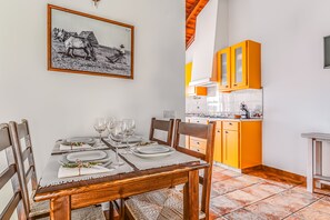 A dining table set with plates, glasses, and a centerpiece. There is a kitchen with orange cabinets and a tiled floor.