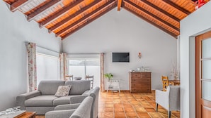 Een ruime woonkamer met een hoge plafond, grijze banken, een eettafel en een aan de muur bevestigde televisie.