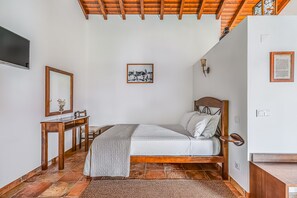 A bedroom with a bed, wooden desk, and a wall-mounted TV.