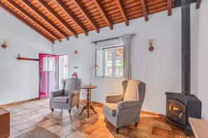 A room with a wooden ceiling, a fireplace, two armchairs, a small round table, and a door with a pink frame.