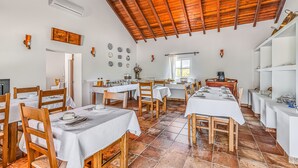 Un comedor con varias mesas, sillas de madera, manteles blancos y piso de baldosas.