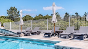 A swimming pool with lounge chairs and umbrellas, surrounded by a fence and greenery. - Apartment 'Casa Ti Herminia - Suite Deluxe' with Shared Pool, Wi-Fi and Air Conditioning (Carvalhal)