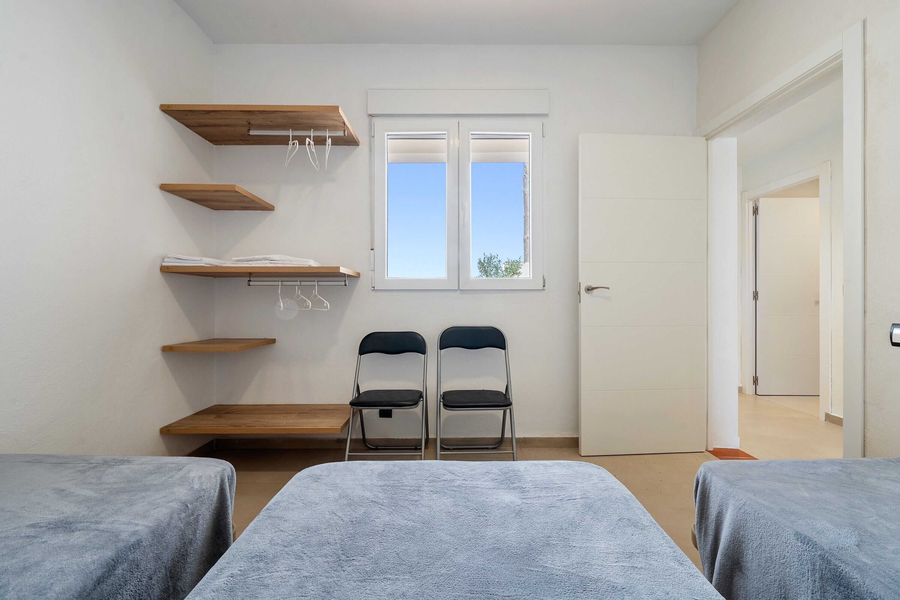Una habitación con dos camas, estanterías de madera, una ventana y una puerta.