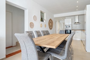 Un'area pranzo moderna con tavolo in legno e sedie rivestite di grigio, una cucina con elettrodomestici bianchi e decorazioni a parete.