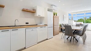 Una cocina moderna con armarios blancos, encimera de madera y comedor con sillas grises y mesa de madera.