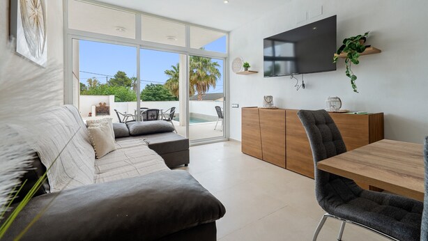 Una sala de estar moderna con un sofá, una mesa de comedor y un televisor montado en la pared.