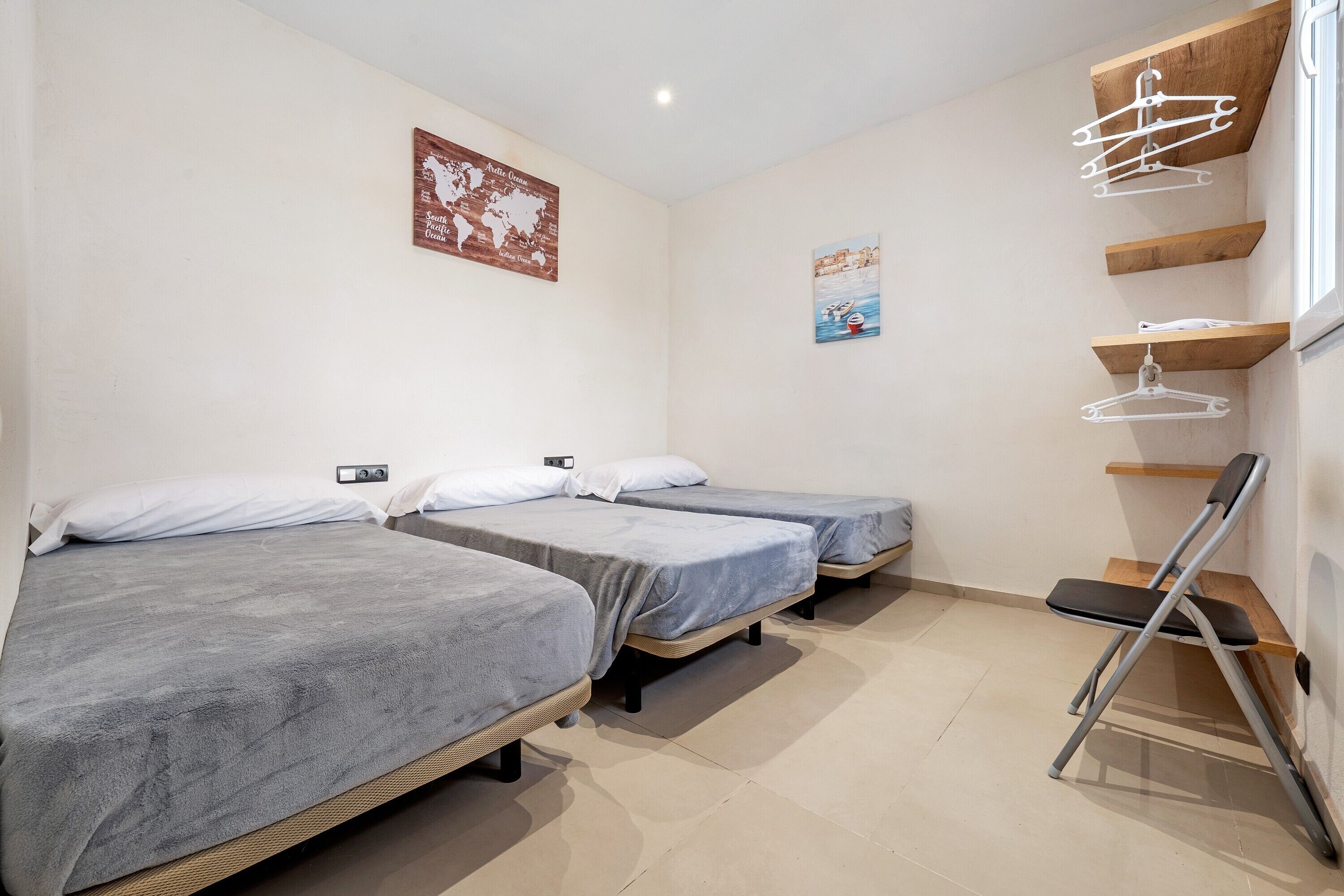 A room with three beds, a wooden shelf, and a wall-mounted hanger rack.