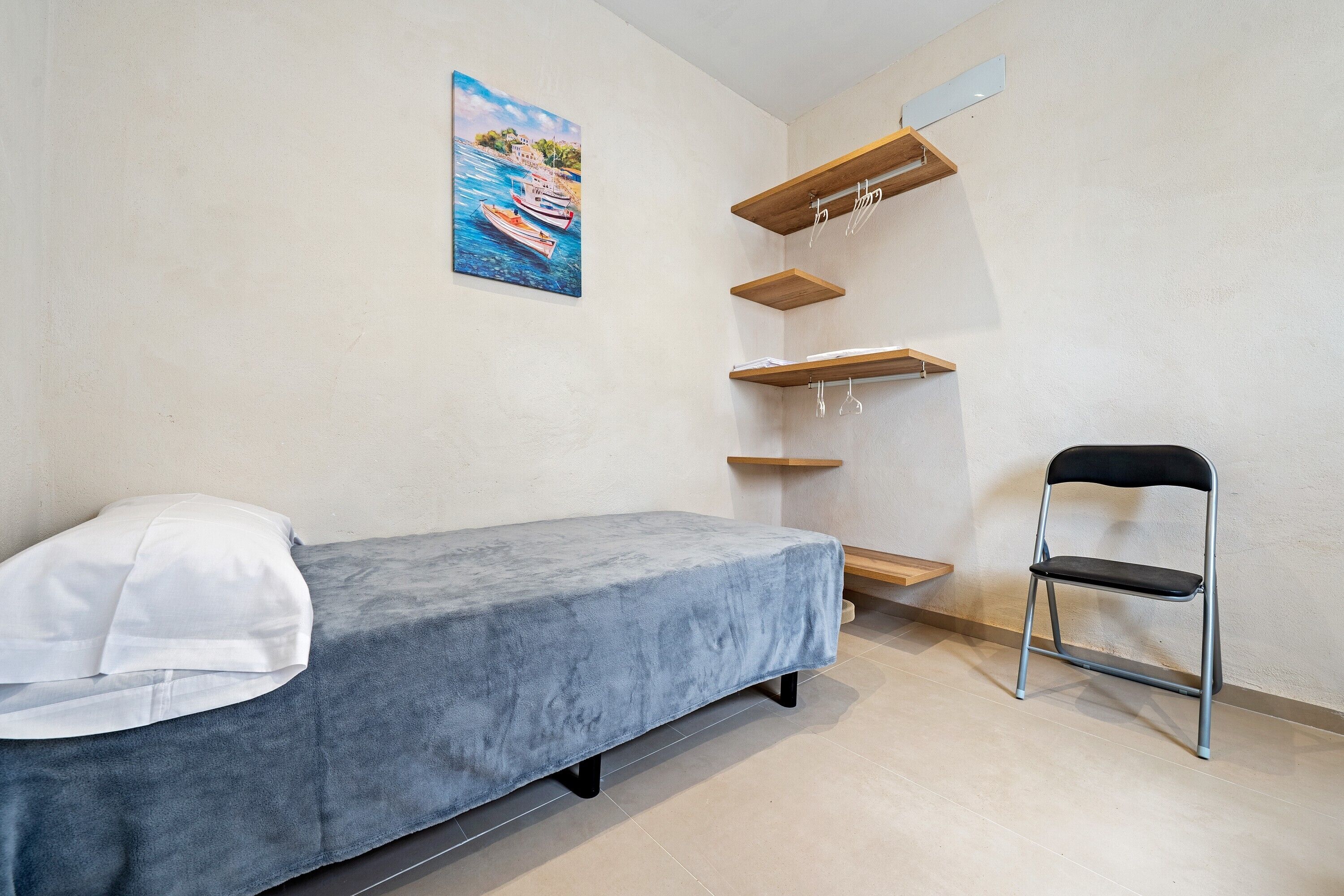 Una habitación pequeña con una cama individual, una silla y estanterías de madera en la pared.