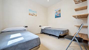A room with two beds, a desk, and a chair. There are wall-mounted shelves and a hanging coat rack.