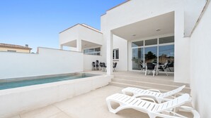 Zona de piscina exterior moderna amb gandules, un porxo tancat amb vidre i un cel blau i clar.