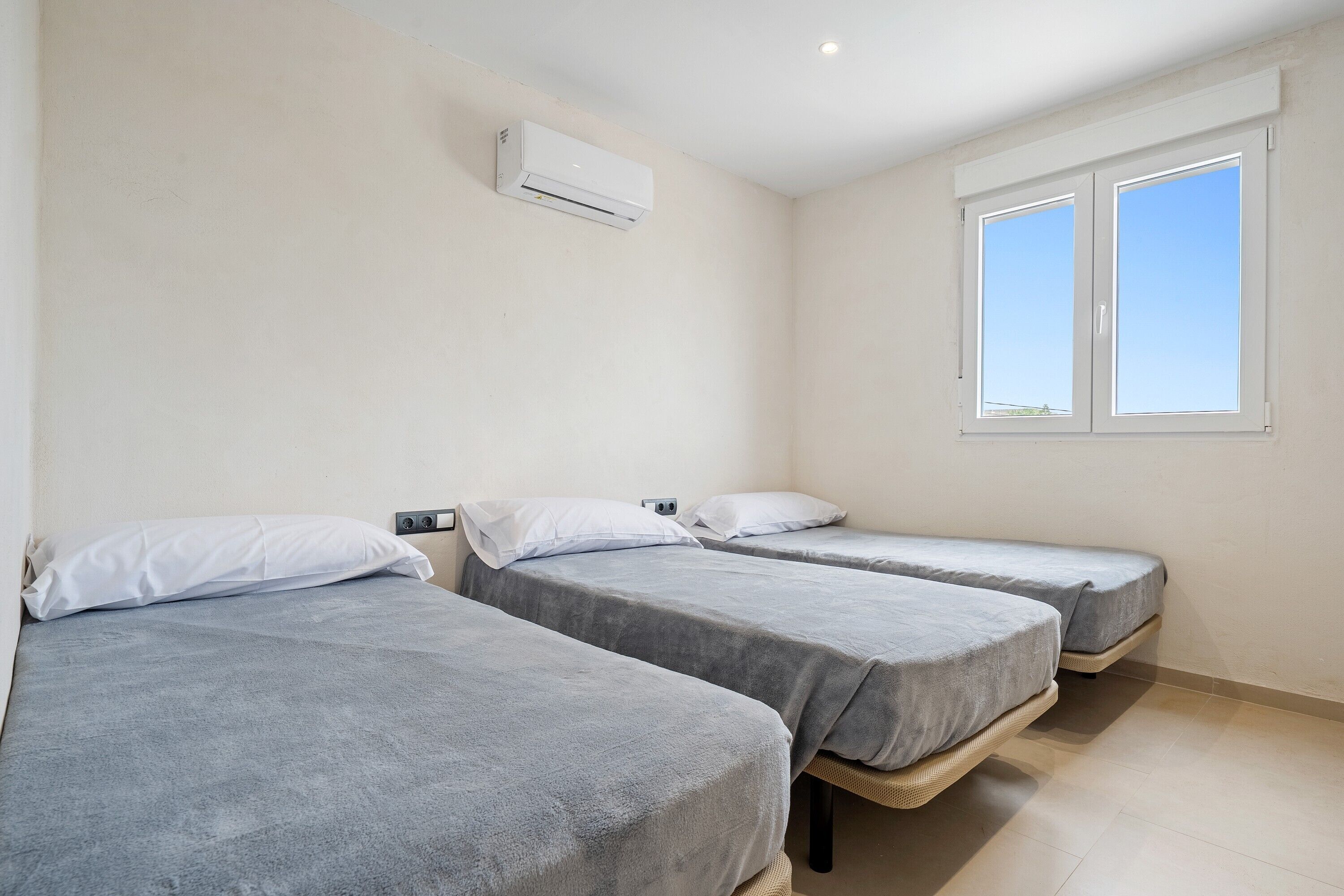 A room with three single beds, a window, and an air conditioning unit.