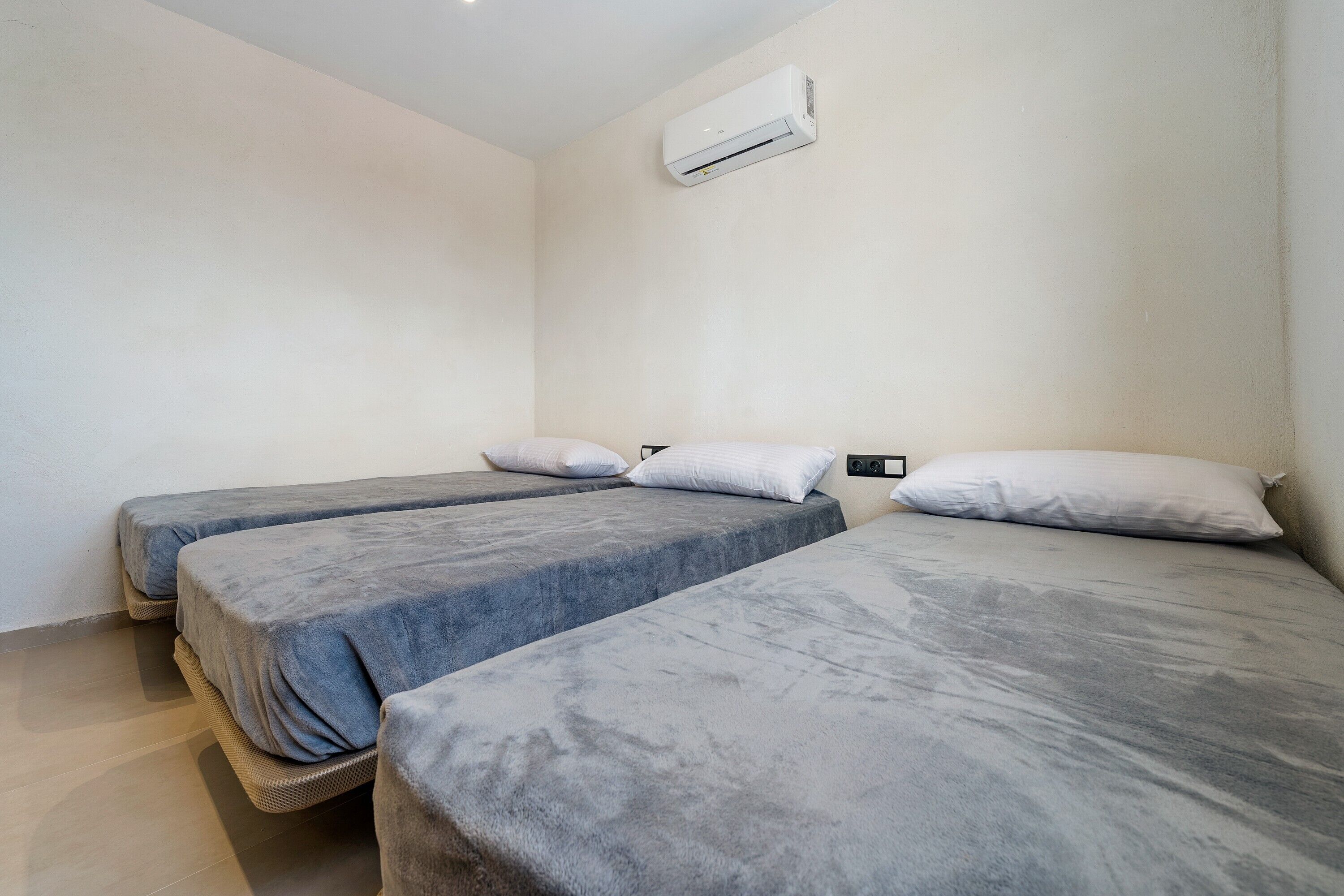 Ein Zimmer mit drei Betten, einer Wandklimaanlage und einer Steckdose.