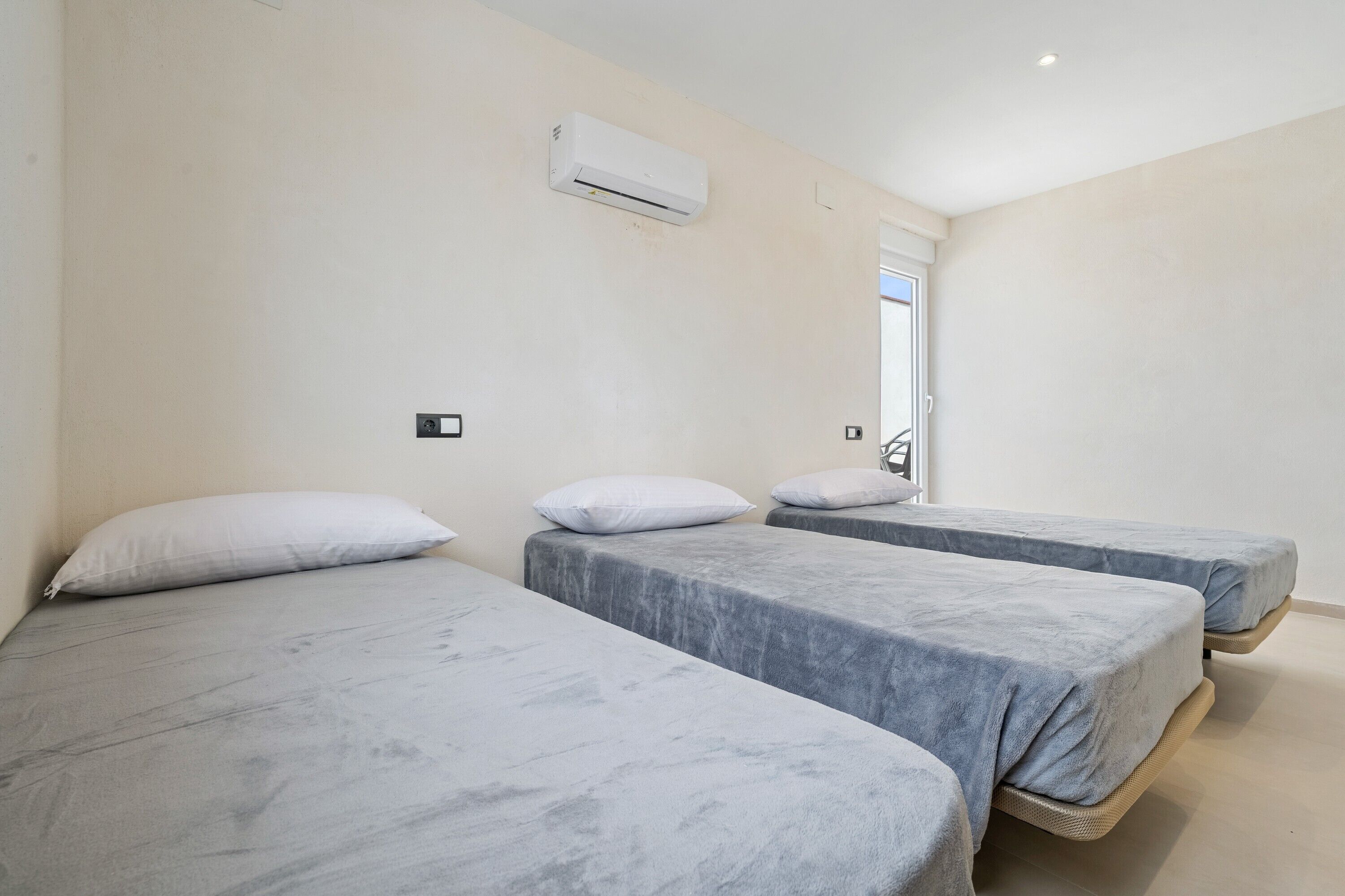 Una habitación con tres camas, un equipo de aire acondicionado blanco y una puerta.