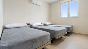 Une chambre avec trois lits, un appareil de climatisation, une fenêtre et un interrupteur sur le mur.