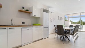 Une cuisine moderne avec des meubles blancs, un lave-vaisselle, un réfrigérateur et un coin repas comprenant une table et des chaises.