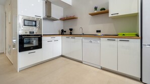 Une cuisine moderne avec des meubles blancs, un four encastré, un lave-vaisselle et des plans de travail en bois.
