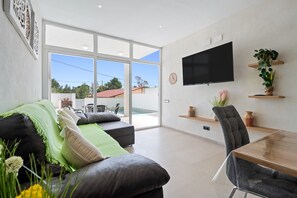Ein modernes Wohnzimmer mit einer Couch, einem Esstisch, einem Fernseher und einem großen Fenster.