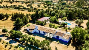 A rural property with a main building, a swimming pool, and surrounding greenery.