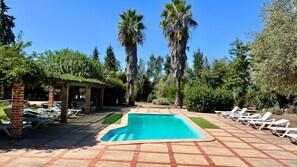A swimming pool with lounge chairs, a covered patio area, and surrounding trees.