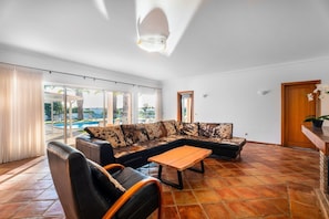 Una sala de estar con un sofá, una mesa de centro y una silla. Se ve una piscina a través de las puertas de vidrio.