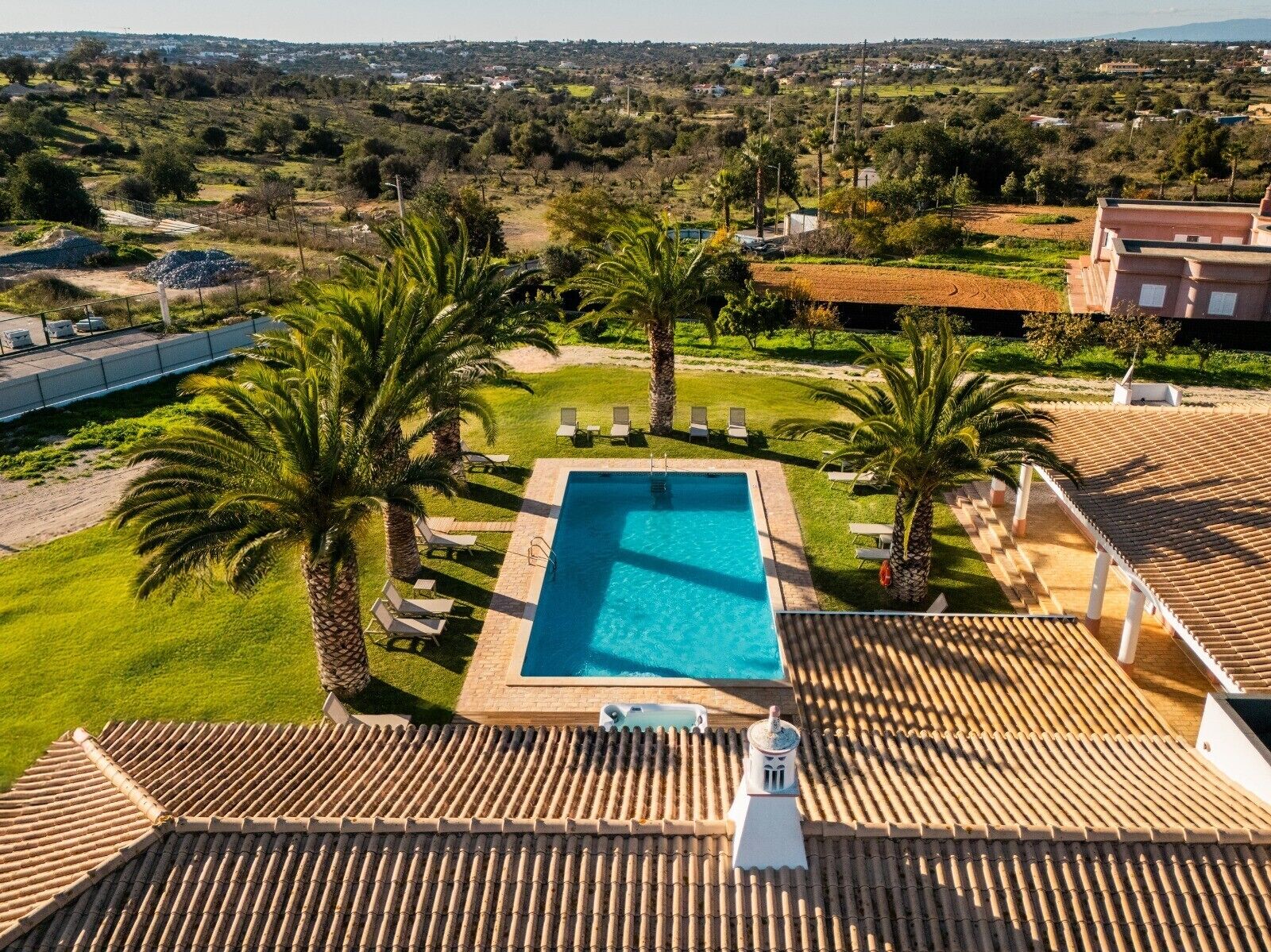 A rooftop pool with a clear view of the surrounding landscape, including palm trees and a distant town.