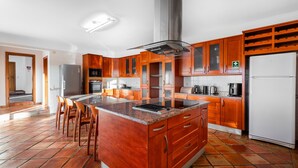 Une cuisine moderne avec des meubles en bois, un îlot central, des appareils électroménagers en acier inoxydable et un sol carrelé.