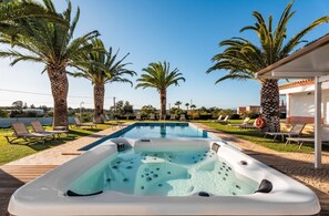 A swimming pool with lounge chairs, a hot tub, and palm trees.
