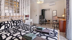 A bedroom with a patterned bedspread, a desk, a chair, a mirror, and a window with a view of trees.