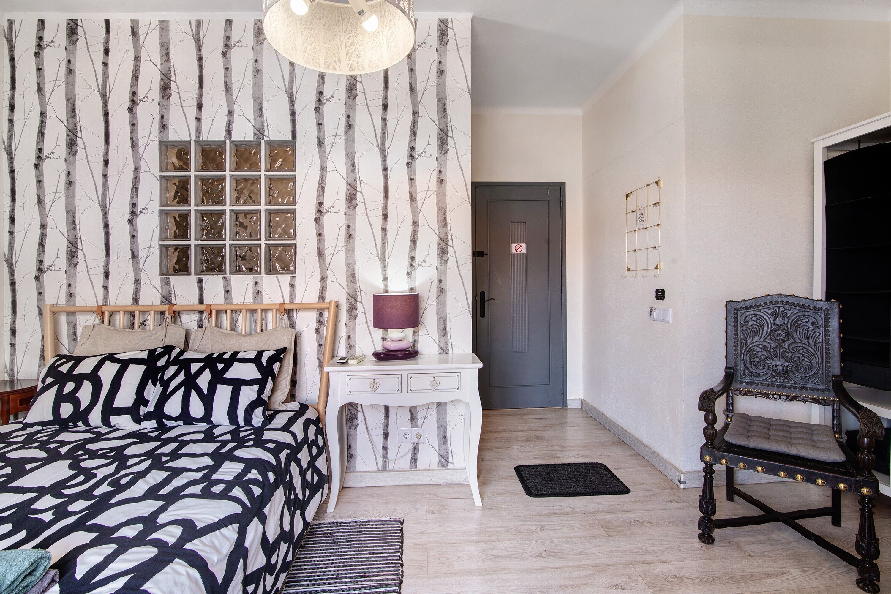A bedroom with a bed, bedside table, lamp, chair, and a door.