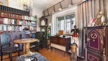 A room with a large bookshelf, a wooden cabinet with decorative items, a round table, and a vintage clock.