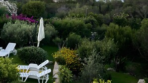 A garden with white lounge chairs, a white umbrella, and a view of the sea and mountains. - Villa 'Viola Con Piscina E Giardino' with Sea View, Private Pool and Wi-Fi (Punta Sardegna)