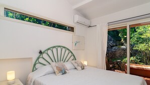 A bedroom with a bed, bedside tables, a window with a view of greenery, and an air conditioning unit. - Villa 'Viola Con Piscina E Giardino' with Sea View, Private Pool and Wi-Fi (Punta Sardegna)