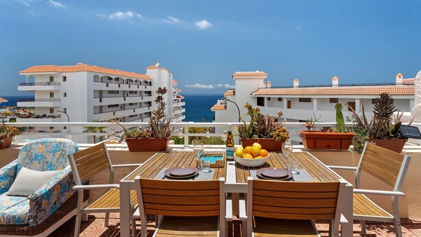 A terrace with a wooden table, chairs, and potted plants. - Vacation 'Ocean Sun' with Sea View, Shared Pool and Wi-Fi (Puerto de Santiago)