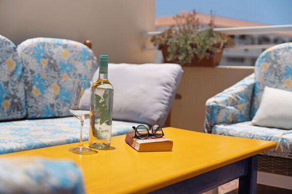 A yellow table with a bottle of El Cacique, a glass, and a book with glasses on it, placed on a blue floral sofa.