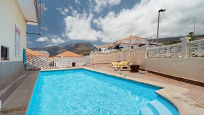 A swimming pool with a view of mountains, a white fence, and a street lamp. - Vacation 'Ocean Sun' with Sea View, Shared Pool and Wi-Fi (Puerto de Santiago)