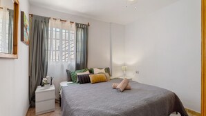 A bedroom with a bed, nightstand, curtains, and a window. - Vacation 'Ocean Sun' with Sea View, Shared Pool and Wi-Fi (Puerto de Santiago)