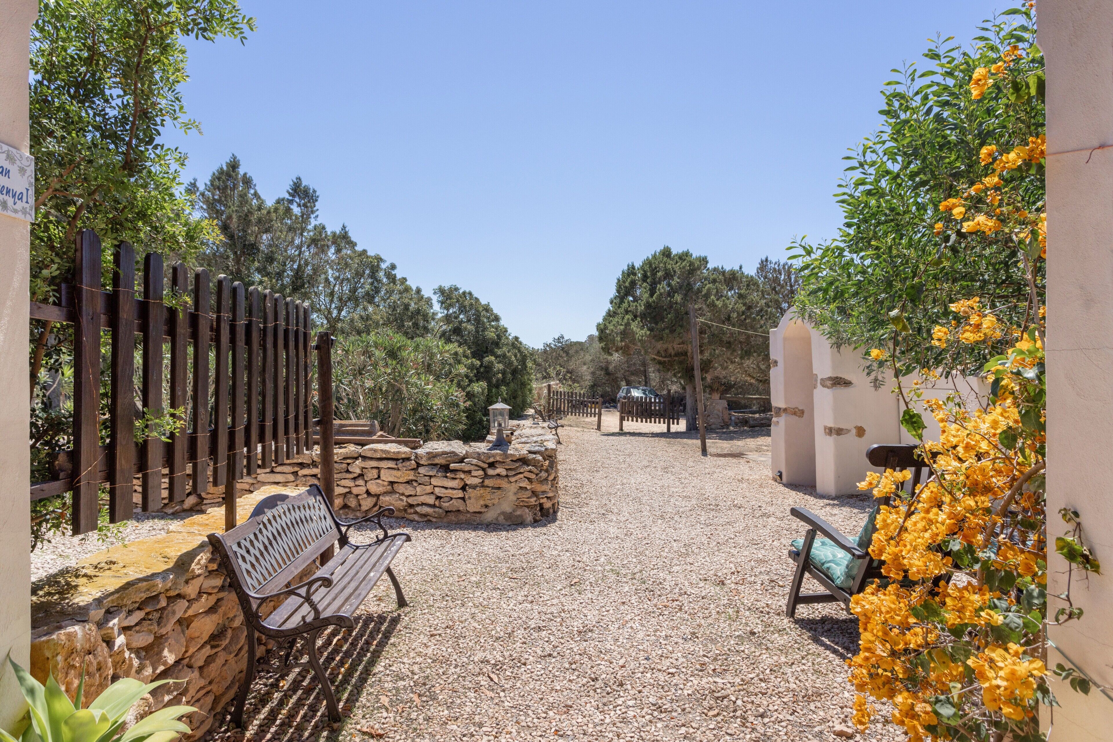 A gravel courtyard with a wooden fence, a stone wall, and a bench.