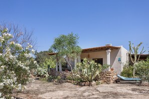 Un edificio rústico con pared de piedra, puerta de madera y una silla de lounge azul en primer plano.