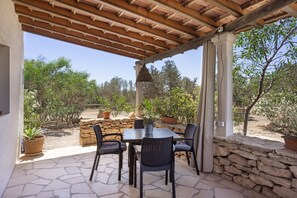 Un patio al aire libre con una mesa y sillas de piedra, rodeado de plantas en macetas y un muro de piedra.