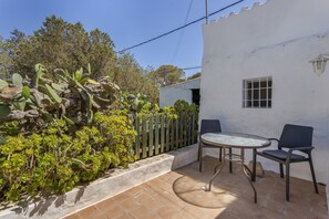 Un patio con una mesa redonda y dos sillas, una pared blanca y una valla de madera.