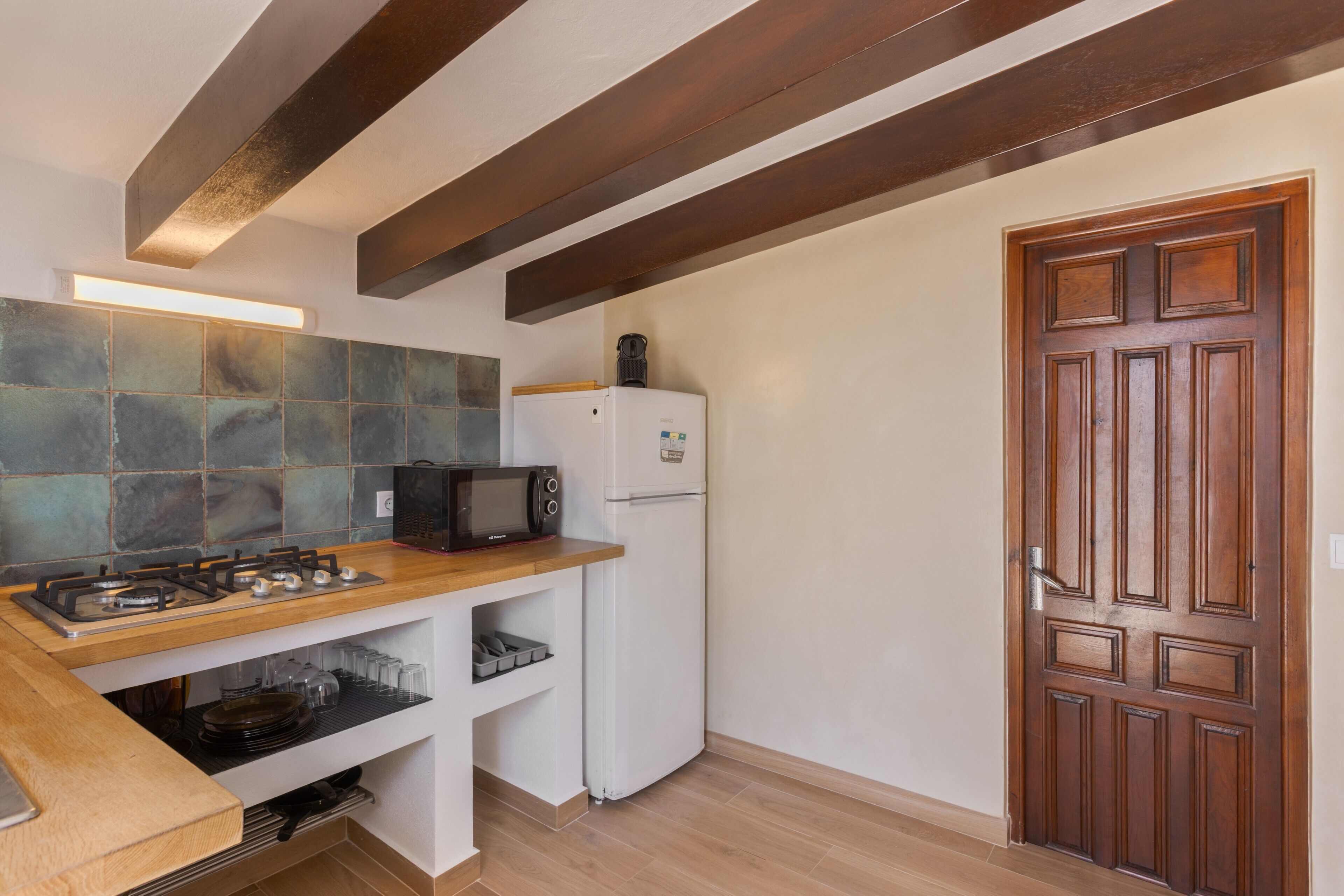 Una cocina con estufa a gas, microondas y refrigerador, vigas de madera en el techo y una puerta de madera.