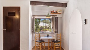 Une pièce avec une porte en bois, une fenêtre avec des rideaux, une table avec deux chaises, un luminaire suspendu et une petite étagère au-dessus de la fenêtre.