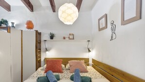 Un lit bien fait, avec des serviettes, une tête de lit en bois, un luminaire suspendu et une étagère avec des livres et une plante.