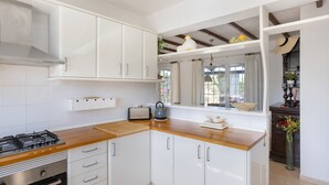 Une cuisine avec des meubles blancs, un plan de travail en bois, une cuisinière à gaz et une fenêtre avec des rideaux.