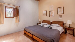 Une chambre à coucher avec un lit en bois, une fenêtre avec des rideaux, une table de chevet et des œuvres d’art accrochées au mur.